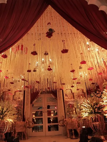 A grand entrance framed by red velvet curtains and an elaborate ceiling of hanging floral strings, creating a dramatic and opulent welcome for guests.