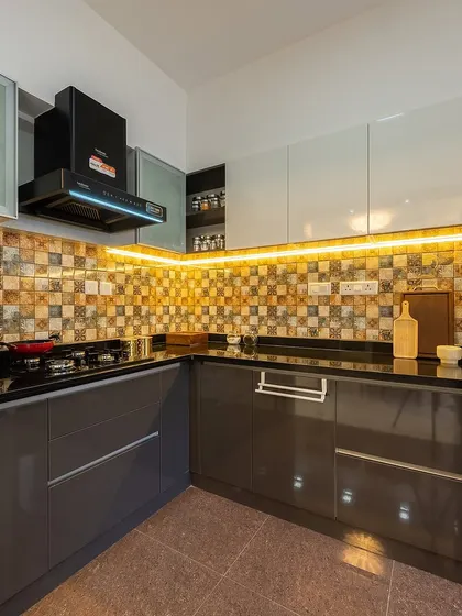 The kitchen in this Bangalore home is a mix of glossy grey cabinets, a patterned tile backsplash, and warm under-cabinet lighting.