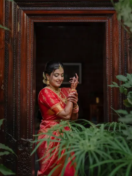 A portrait of the bride in her stunning red saree, framed by the rustic charm of her wedding venue. We focus on creating images that are both beautiful and full of character.