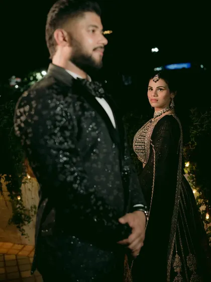 A dramatic, moody portrait of the couple at night, with the groom in the foreground and the bride looking towards him.
