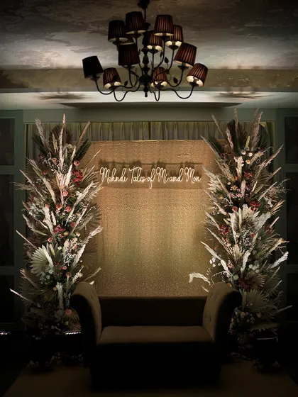 A moody and rustic stage setup for an intimate event, featuring dried pampas grass arrangements and a custom neon sign.