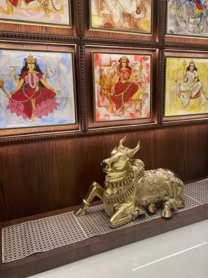 This pooja space features a gallery wall of beautifully framed deities, creating a powerful spiritual center. The brass Nandi statue in front adds a traditional and devotional touch, grounding the space with its presence.