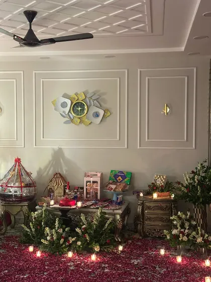 A decorated corner of the room showing gift hampers and arrangements. The floor is covered in rose petals and lined with candles, adding to the celebratory feel.