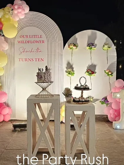 This "little wildflower" theme for Sharbodita's 10th birthday is both sweet and sophisticated. The setup features clean white backdrops, a beautiful pink and yellow balloon arch, and marquee numbers, creating a lovely nighttime celebration.