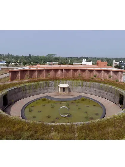 This image shows the relationship between the subterranean memorial gallery and the main auditorium building. The green roof of the gallery acts as a natural foreground, blending the structure into the landscape of Mysore.