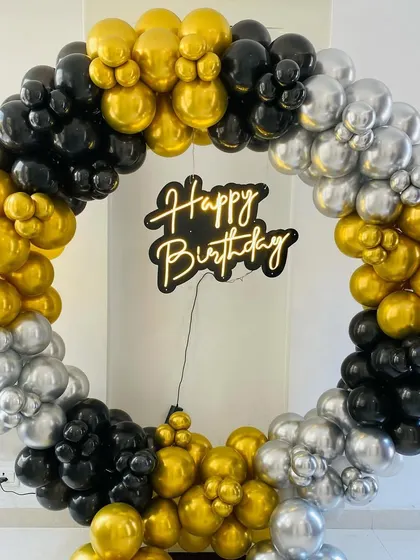 A full balloon ring in black, gold, and silver with a "Happy Birthday" neon sign.