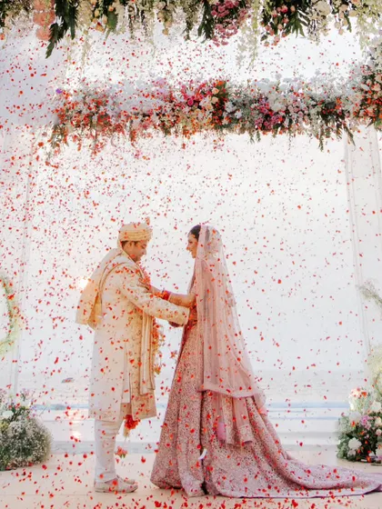A magical moment as the couple exchanges garlands under a shower of red rose petals at their beach wedding. This is a classic, must-have shot.