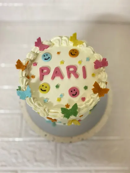 A top-down view of this cheerful vanilla cake, decorated with colourful smilies and butterflies for Pari.