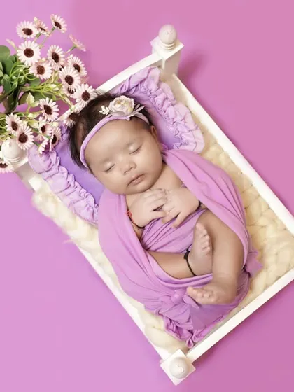 A beautiful overhead shot of a newborn swaddled in lavender. The simple composition on a solid background emphasizes the baby's peaceful pose.