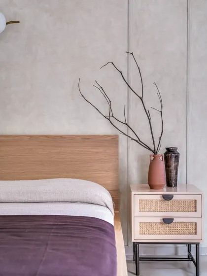 A detail shot of the autumnal master bedroom, focusing on the contrast between the dark wood, the cane nightstand, and the textured wall. The dried branches add a sculptural, natural element.