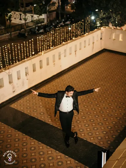 The groom striking a pose on a terrace decorated with string lights, a fun reception shot.