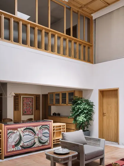 **Cocoon House, Ahmedabad:** A hand-painted console table serves as a vibrant focal point, introducing traditional art into the modern interior. The upper-level wooden railing creates a visual connection between floors, enhancing the sense of an open, interconnected home.