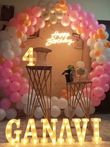 A fourth birthday party decoration in pink and white. This setup includes a circular balloon arch, a neon sign, and large light-up marquee letters for the name.