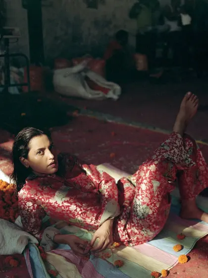 A full-length shot capturing a relaxed pose amidst the flower market. The styling of the printed co-ord set against the colorful floor mat and piles of flowers creates a grounded, yet highly fashionable, composition.