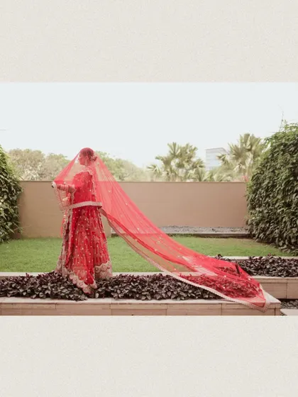 The bride plays with her long red veil in the garden, creating a dynamic and beautiful image.