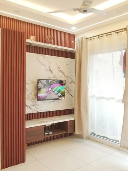 A living room featuring a TV unit with a marble back panel and reddish-brown fluted accents. The design cleverly integrates a pooja unit into the overall wall feature.