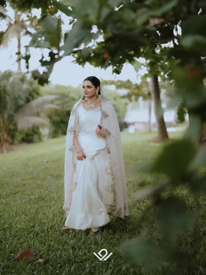 A bride in a beautiful white outfit walks through a park, a candid moment captured in a natural setting.