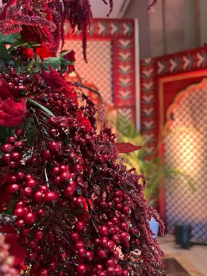 A close-up of a lush floral arrangement with red berries and roses, with a traditional patterned backdrop in the distance.