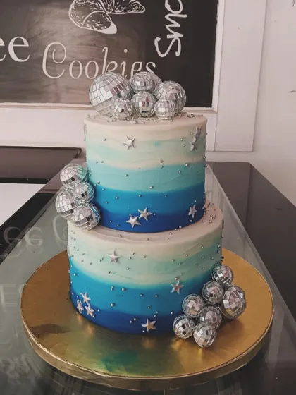 A cool and groovy disco-themed cake. This two-tiered design has a blue ombre effect and is decorated with silver stars and sparkling disco balls.