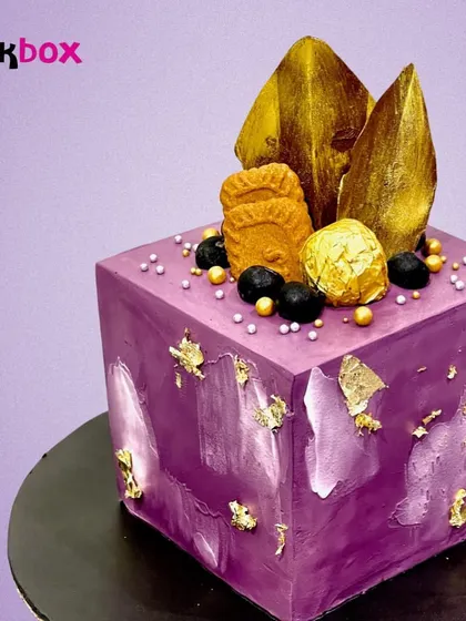 We were asked to create something "out of the box," so we made this purple cube cake. It's an abstract, modern design topped with Biscoff cookies and gold leaf for a truly unique celebration.