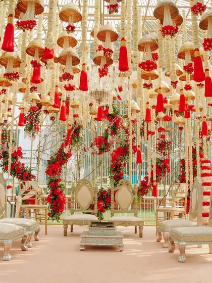 A breathtaking mandap decorated with hanging red tassels, temple bells, and strings of white flowers. The design is a beautiful tribute to traditional Indian craftsmanship and festive colors.