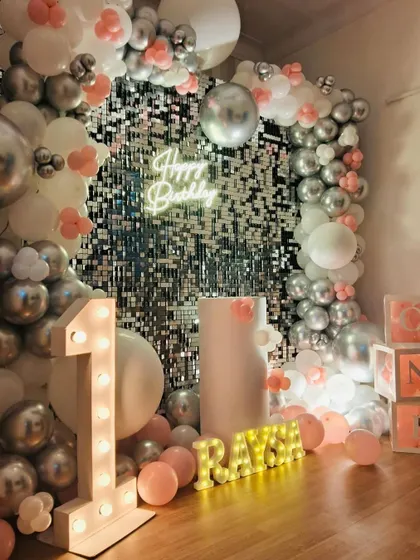 A first birthday is a precious milestone. We designed this beautiful setup for baby Raya's big day, featuring a silver sequin wall, a soft pink and white balloon arch, and light-up letters spelling out her name for a personal and adorable touch.