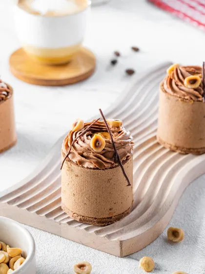 An exquisite hazelnut and chocolate mousse dessert, styled with a minimalist aesthetic. The focus is on the intricate piping work and delicate decorations, showcasing the artistry of the pastry chef on a clean, white background.