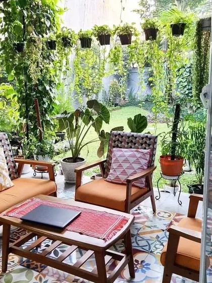 This patio design features a comfortable outdoor sofa and chairs with colorful cushions. The space is surrounded by a lush garden with hanging plants, creating a private and relaxing atmosphere for homeowners.