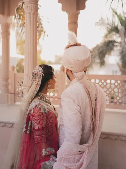 A quiet moment shared between the bride and groom, standing together against a backdrop of elegant architecture. This shot captures their connection from a respectful distance.