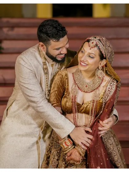 A warm and affectionate portrait of the couple, with the groom embracing the bride from behind, both sharing a genuine smile.
