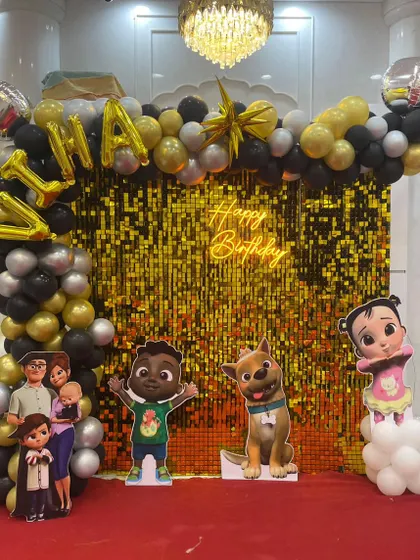A Cocomelon themed birthday party featuring a gold shimmer wall, black and gold balloon arch, and cutouts of the entire Cocomelon family.