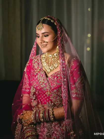 A happy bride captured in a candid moment. Her hair is pulled back into a neat bun, allowing her heavy necklace, maang tikka, and nath to be the stars of the show.