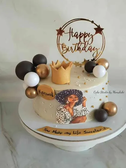 A popular and stylish design for a woman's birthday. This no-fondant cake features a chic illustration, a golden crown, and a black, white, and gold balloon garland.