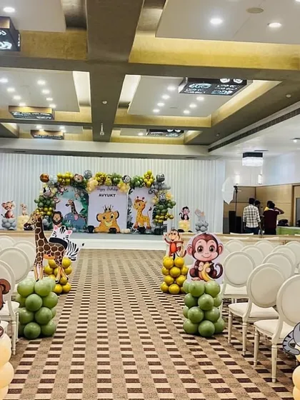 A full view of a banquet hall decorated for a jungle theme birthday. The setup includes a main stage backdrop, and the walkway is lined with balloon pillars topped with cute animal cutouts like bears, cats, and monkeys.