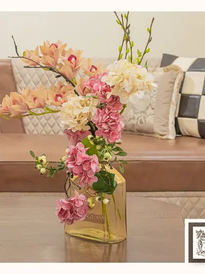 This coordinated floral arrangement in a golden glass vase adds a touch of sophistication to this living room. The soft pinks and creams complement the leather sofa and decorative pillows perfectly.