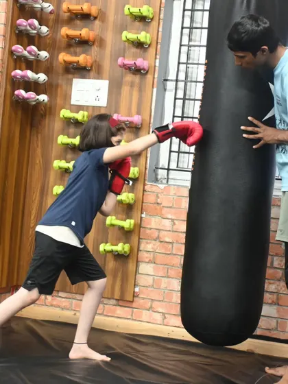 A young girl practicing her boxing on the heavy bag under the guidance of a coach. We are committed to empowering the next generation of female fighters.