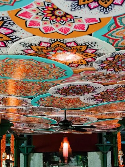A creative ceiling treatment for a Mehendi function. The ceiling is covered with colorful, mandala-printed discs, adding a unique artistic touch to the decor.