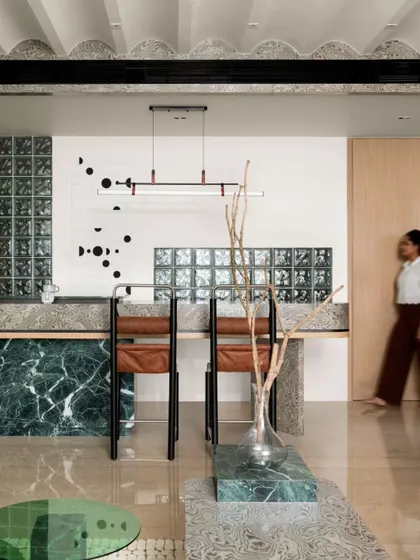 The breakfast counter, with its green marble base and textured veneer top, is a visual focal point. The custom wall art and glass block backdrop add layers of interest, turning a functional area into a design statement.