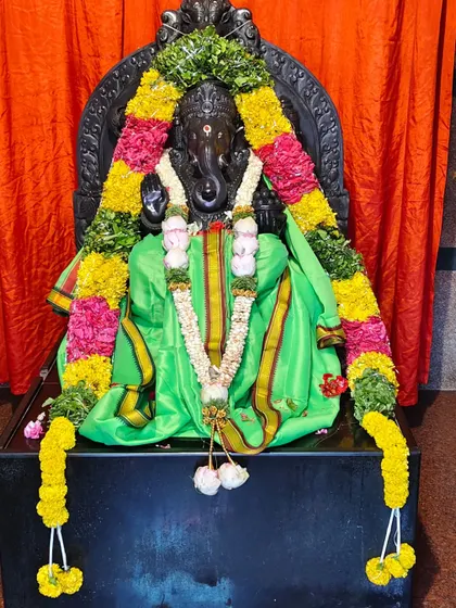 The idol of Lord Ganesha adorned with a green silk cloth and a long, colorful flower garland.