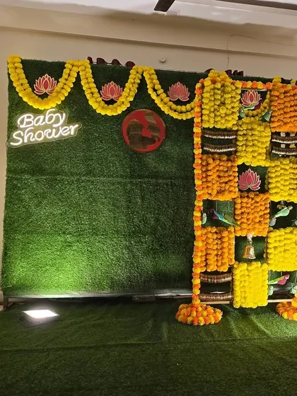 A traditional marigold and lotus themed baby shower backdrop with a neon sign, before the seating is placed.