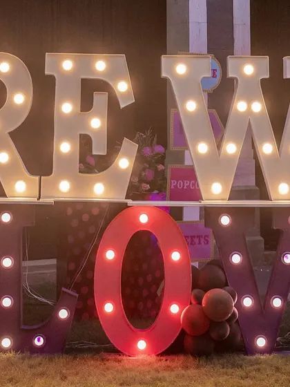 Another angle of the 'HERE WE GLOW' marquee sign, a key decorative element for the neon-themed event.