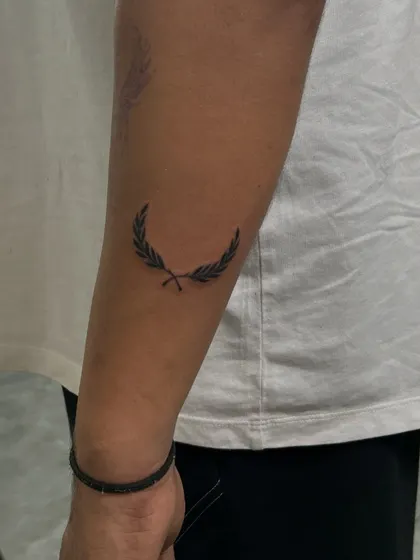 A simple and elegant laurel leaf tattoo on the forearm. This minimalist design is a classic symbol of victory and honor, created with delicate, clean lines.