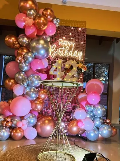 A beautiful 42nd birthday setup with a rose gold shimmer wall and a balloon arrangement in shades of pink, silver, and rose gold.