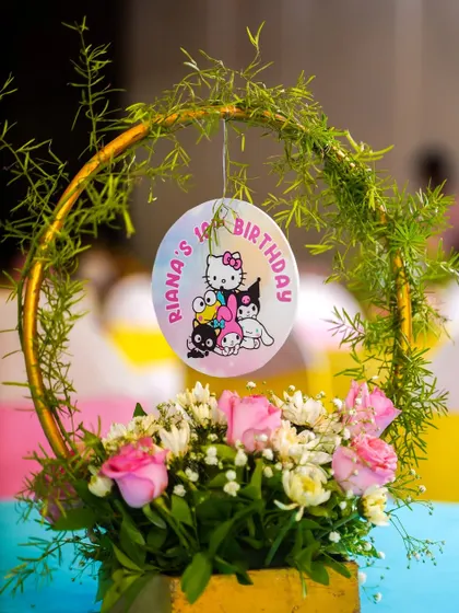 An elegant floral centerpiece with a hanging Hello Kitty themed birthday medallion.