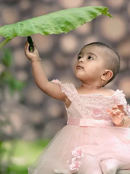 A beautiful, serene portrait of a little girl in a pink dress, looking up at a large leaf. The soft light in our garden is perfect for these gentle moments.