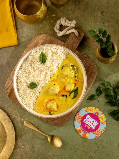 A beautifully composed flat lay of Kadhi Chawal, split yin-yang style in a bowl. The vibrant yellow of the kadhi contrasts with the white rice, garnished with fresh curry leaves for a clean, modern take on a classic comfort food.