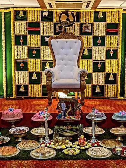 This Seemantham decoration features a checkered backdrop of jasmine and marigold flowers. The stage is filled with an extensive array of decorated plates and traditional dolls.
