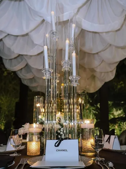 A detailed shot of the tablescape from the Chanel-inspired dinner. A branded gift box sits beside a towering glass candelabra and a lush arrangement of white flowers, showcasing our ability to integrate branding into luxury event decor.