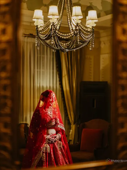 An artistic shot of the bride in her red lehenga, framed in a mirror, creating a sense of mystery and grandeur at the ITC Grand Bharat.