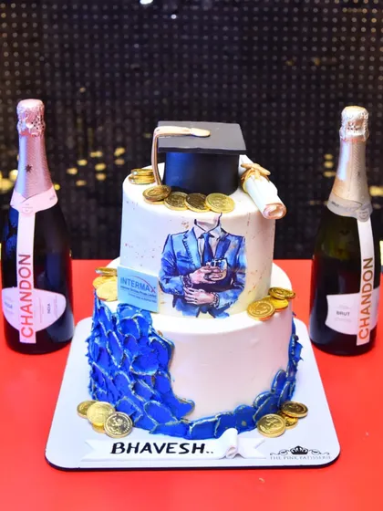 A custom two-tiered cake for a graduation or corporate achievement. The design includes a graduation cap, a diploma, an edible print of the graduate, and a cascade of blue petals and gold coins.